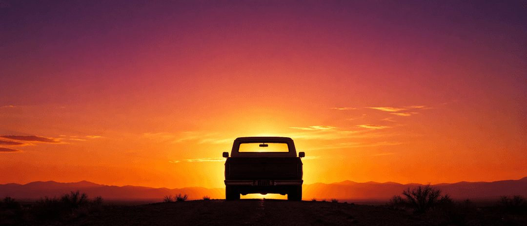 A classic American vehicle parked against a wide blue-hour sky